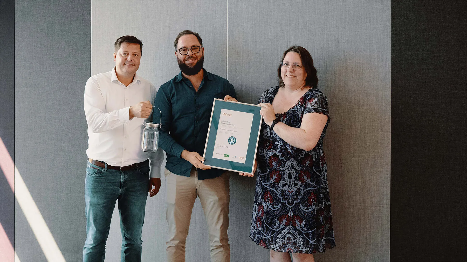 Two men and a woman smile while holding up the framed certification