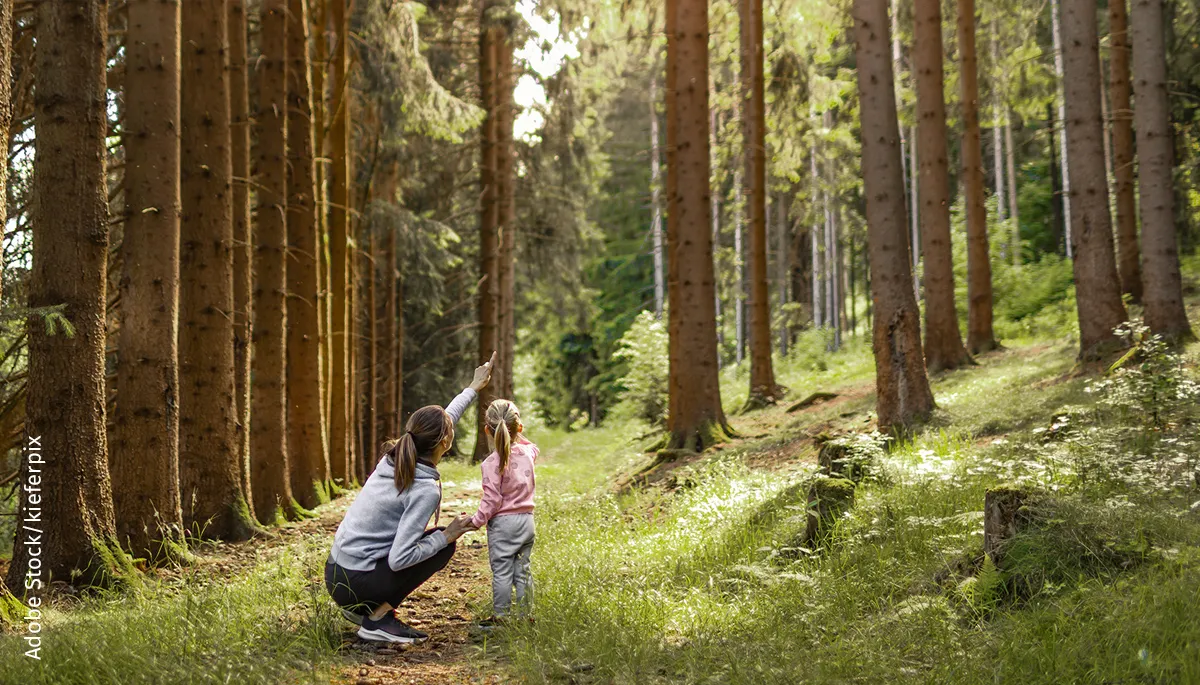 Frau zeigt einem Mädchen etwas im Wald